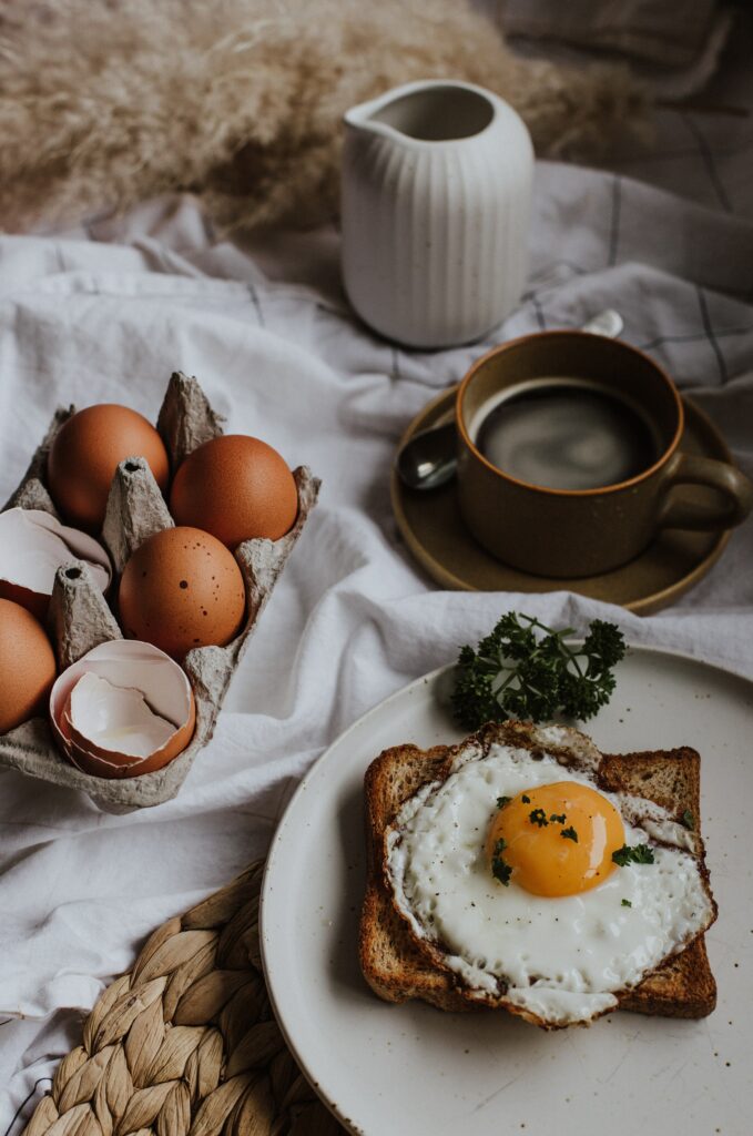Cup of coffee in the background with a carton of six eggs and an egg on toast in the foreground.