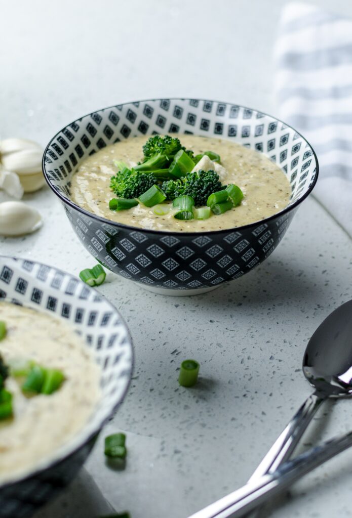 Two bowls of broccoli and cheddar soup with chunks of broccoli and spring onion on top. Two spoons are placed in the foreground.