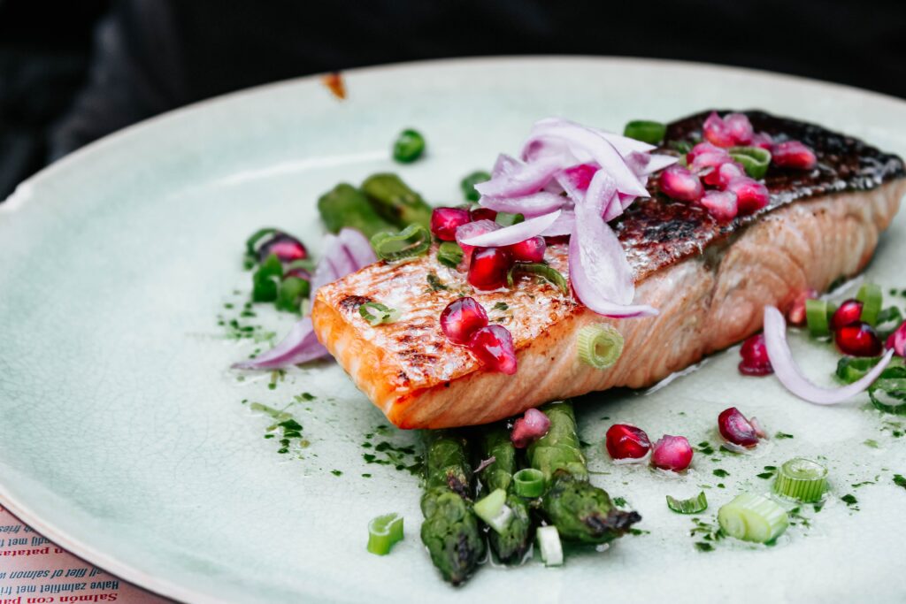 Seared salmon on a blue plate with pomegranate seeds, red onion, and asparagus. 