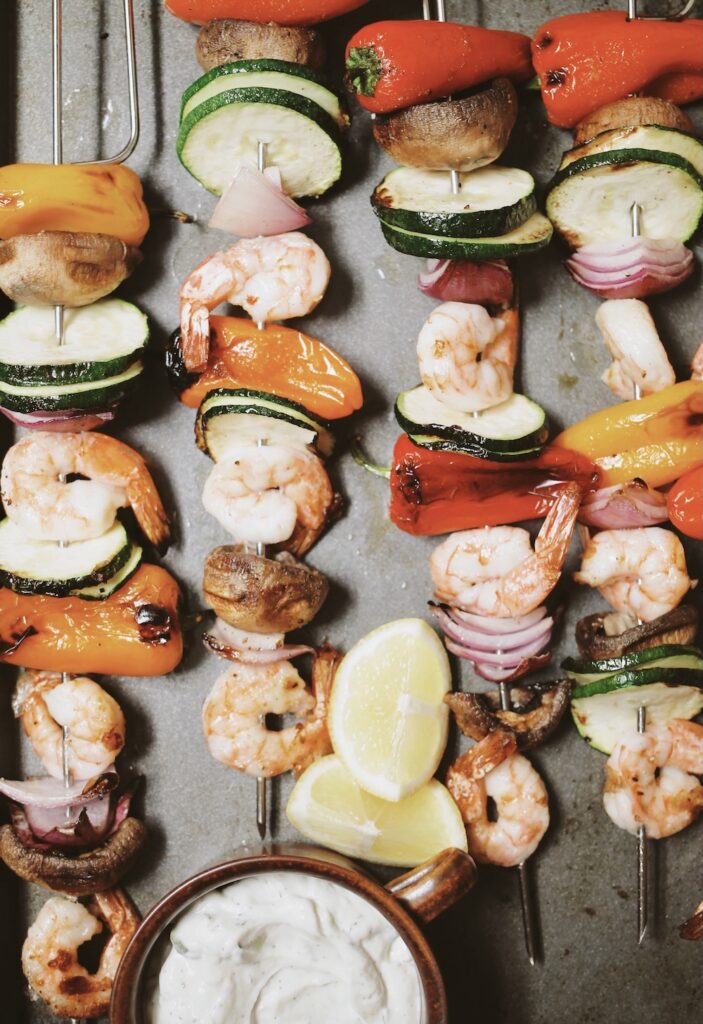 shrimp skewers with colorful veggies and a bowl of tzatziki sauce.