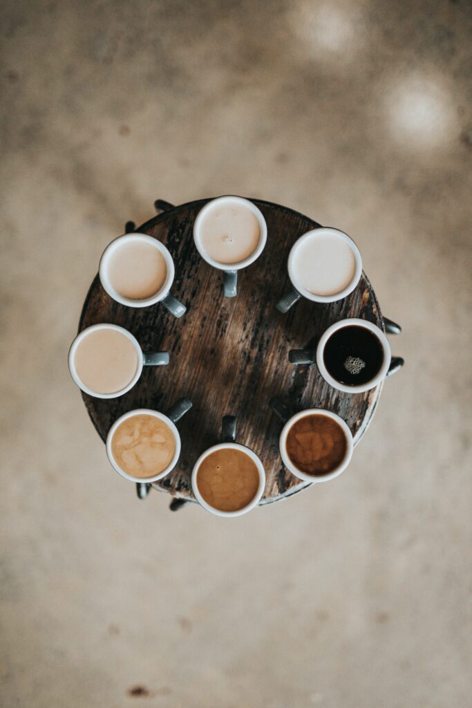 Overhead shot of different mugs of coffee with various coffee drinks, starting with black coffee on the right, around in a circle with more milky coffees.