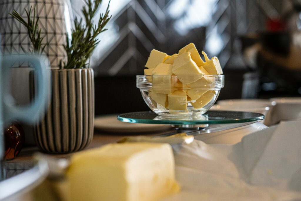 A block of blurry butter is in the foreground. A bowl of cubed butter is in the background.