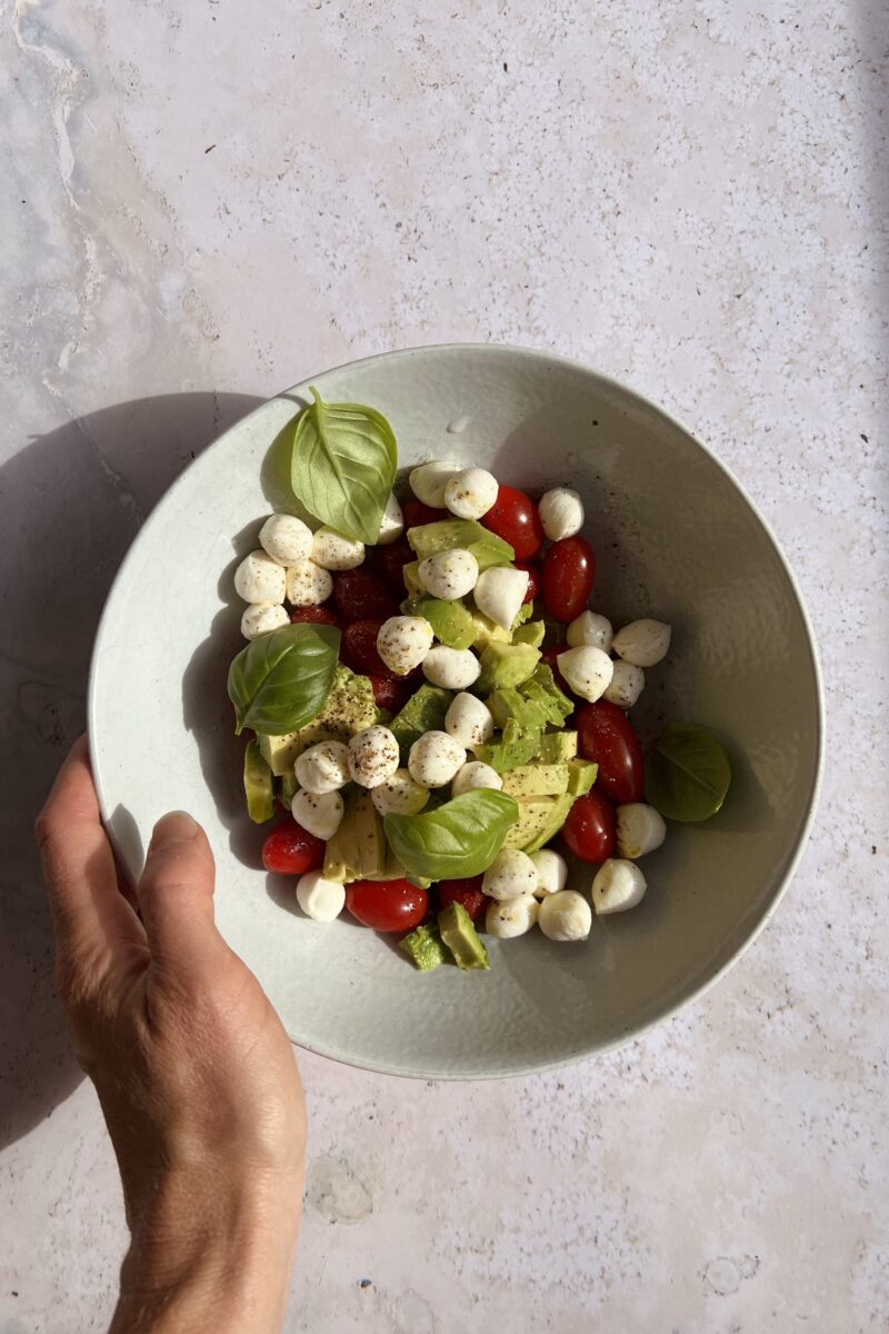 bowl of caprese salad with tomatoes, cheese, avocado, basil, olive oil, sea salt, and pepper
